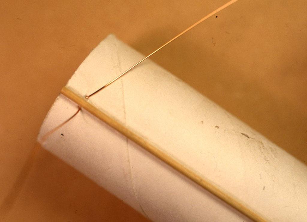 竹串をはさんで紙筒に2カ所穴をあけ、ちょうど竹串の下をくぐらせるように10～ 15 cmくらいエナメノン線を引き出しておいて、巻きはじめを固定します。